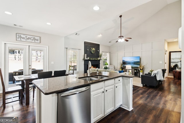 kitchen with a sink, open floor plan, a lit fireplace, dishwasher, and dark stone countertops