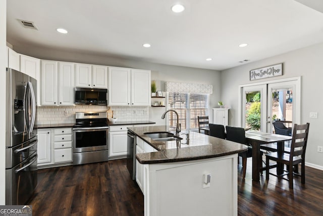 kitchen featuring stainless steel appliances, a sink, visible vents, backsplash, and dark wood-style floors