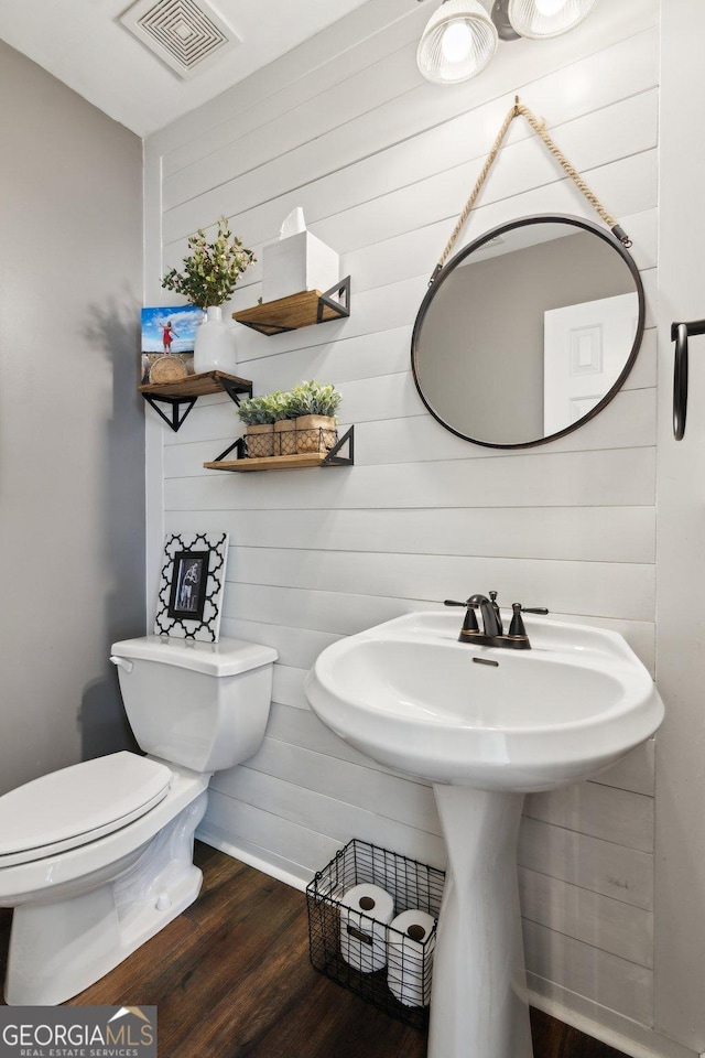 half bath with toilet, visible vents, and wood finished floors