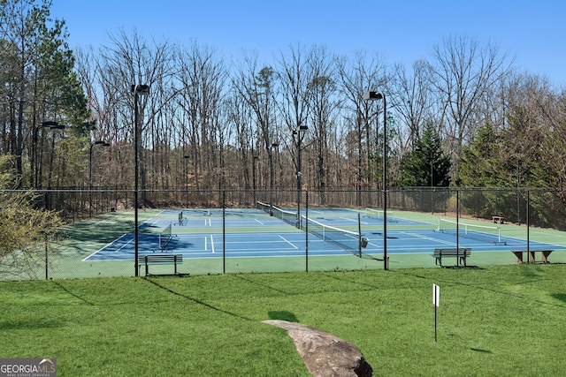 view of tennis court featuring fence and a yard