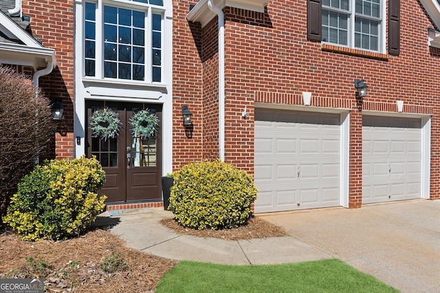 doorway to property featuring an attached garage, brick siding, concrete driveway, and french doors