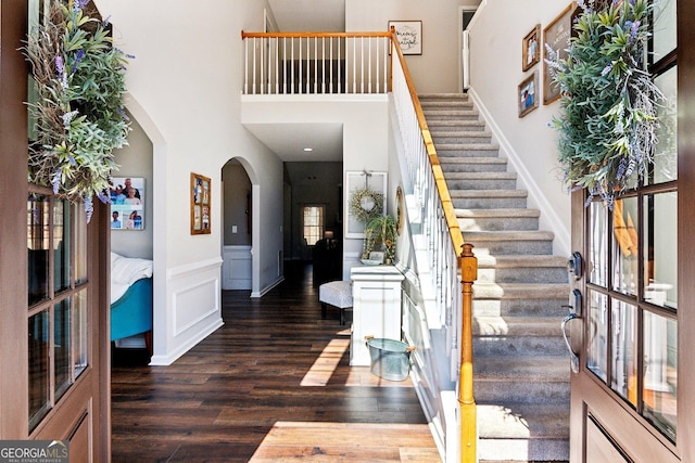 foyer featuring arched walkways, a decorative wall, wood finished floors, stairway, and wainscoting