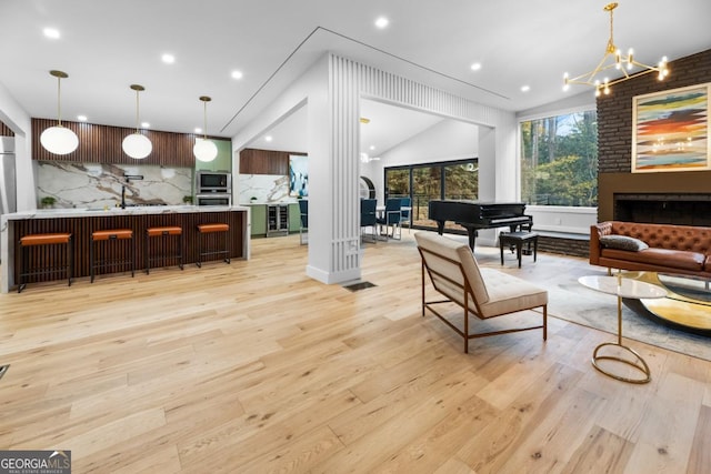 living room with visible vents, vaulted ceiling, light wood-style floors, a fireplace, and a notable chandelier