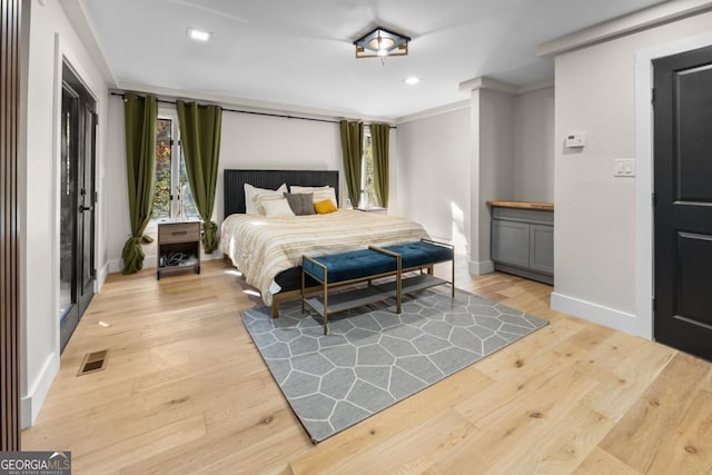 bedroom with ornamental molding, baseboards, visible vents, and light wood finished floors