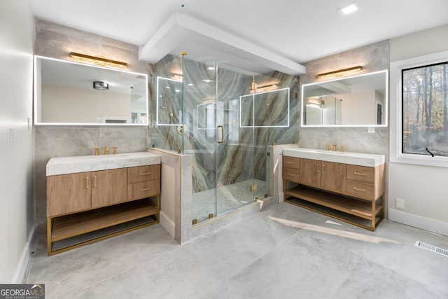 full bath featuring a marble finish shower, two vanities, visible vents, a sink, and baseboards