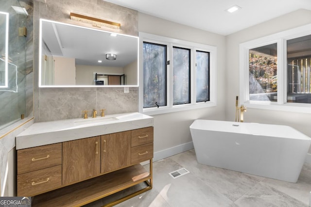 full bathroom featuring baseboards, visible vents, decorative backsplash, a freestanding bath, and vanity