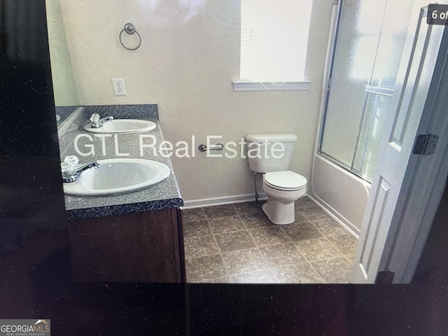 bathroom featuring enclosed tub / shower combo, a sink, toilet, and double vanity