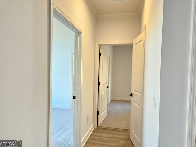 hall featuring light carpet, ornamental molding, light wood finished floors, and baseboards