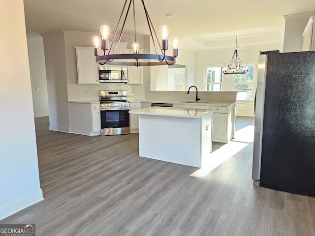 kitchen featuring a chandelier, stainless steel appliances, a sink, a tray ceiling, and crown molding