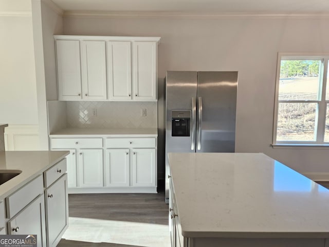 kitchen with wood finished floors, white cabinets, ornamental molding, backsplash, and stainless steel fridge