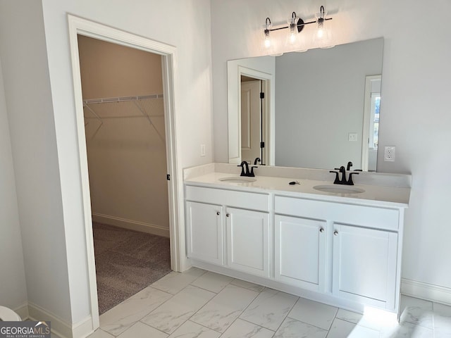 bathroom with double vanity, marble finish floor, a walk in closet, and a sink