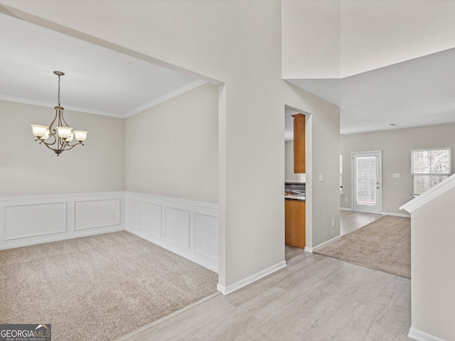 unfurnished dining area featuring light colored carpet, crown molding, light wood finished floors, and an inviting chandelier