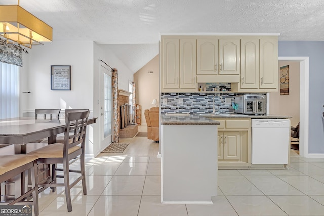 kitchen with light tile patterned floors, cream cabinets, white dishwasher, a sink, and backsplash