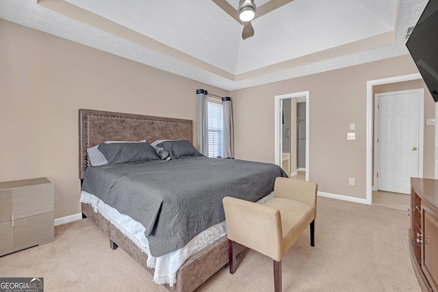 bedroom featuring baseboards, light colored carpet, ensuite bath, ceiling fan, and a tray ceiling