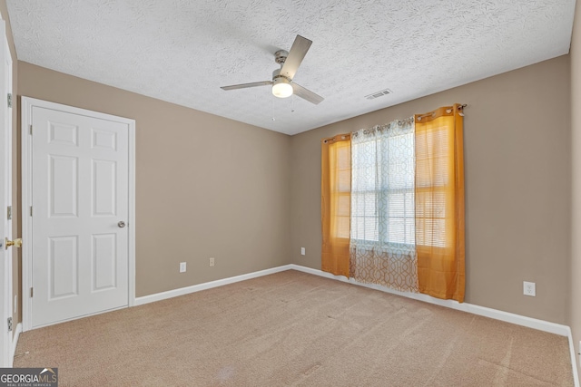 spare room with a textured ceiling, light carpet, a ceiling fan, visible vents, and baseboards