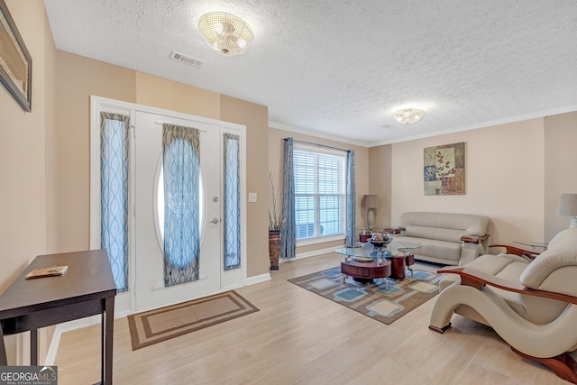 living area featuring baseboards, visible vents, ornamental molding, wood finished floors, and a textured ceiling