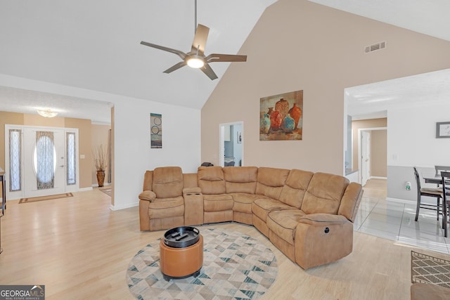 living area with high vaulted ceiling, light wood finished floors, visible vents, and baseboards