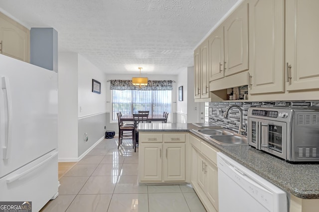 kitchen featuring light tile patterned floors, backsplash, a sink, white appliances, and a peninsula