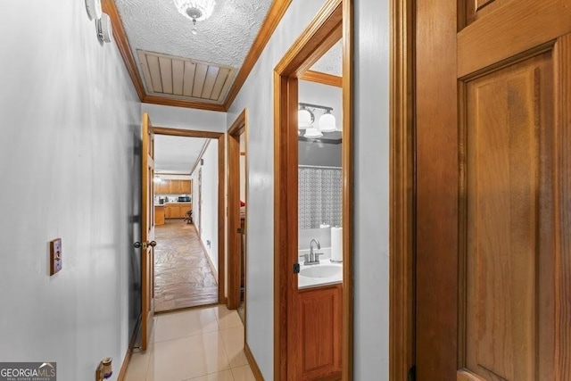 hall with a textured ceiling, light tile patterned floors, a sink, visible vents, and ornamental molding