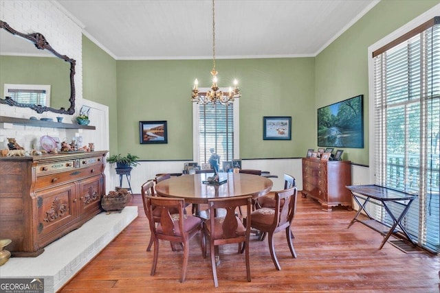 dining area with crown molding, a wainscoted wall, wood finished floors, and an inviting chandelier