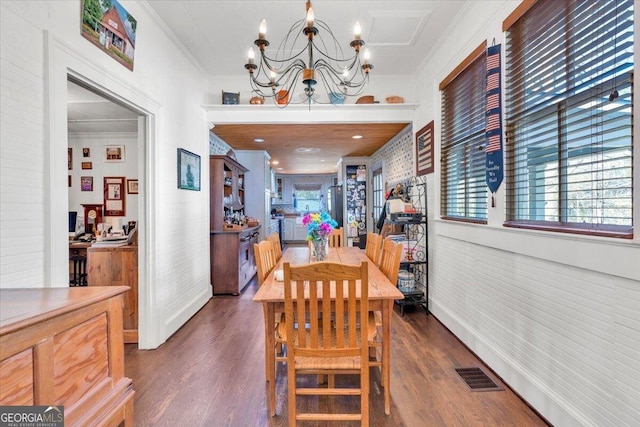 dining space with dark wood-style flooring, visible vents, a chandelier, and crown molding