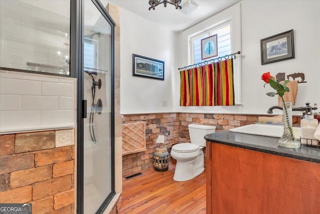 full bathroom with a stall shower, a wainscoted wall, vanity, and wood finished floors