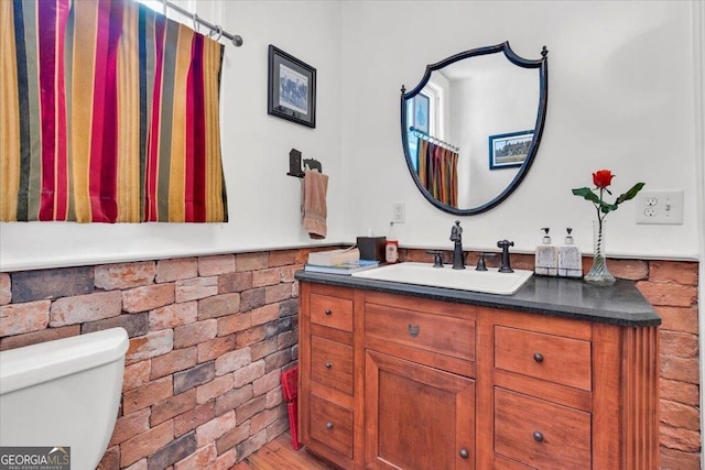 bathroom featuring toilet, brick wall, and vanity