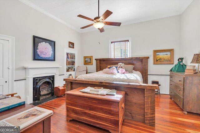 bedroom featuring a fireplace with flush hearth, light wood-type flooring, crown molding, and ceiling fan