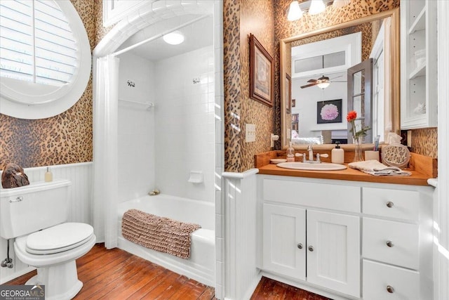 bathroom with shower / washtub combination, toilet, wainscoting, vanity, and wallpapered walls