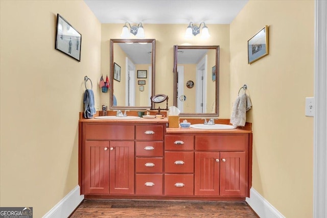 full bath featuring double vanity, a sink, baseboards, and wood finished floors