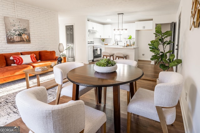 dining space featuring brick wall, wood finished floors, and baseboards