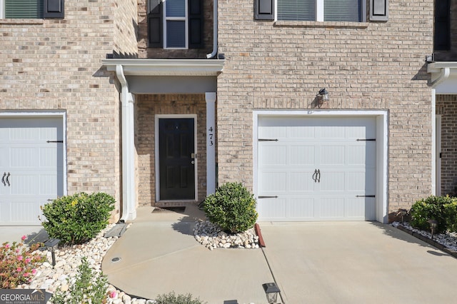 entrance to property with an attached garage, driveway, and brick siding