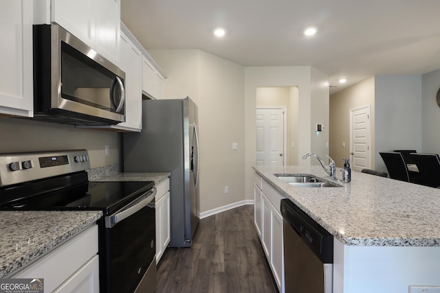 kitchen with white cabinets, dark wood finished floors, an island with sink, stainless steel appliances, and a sink