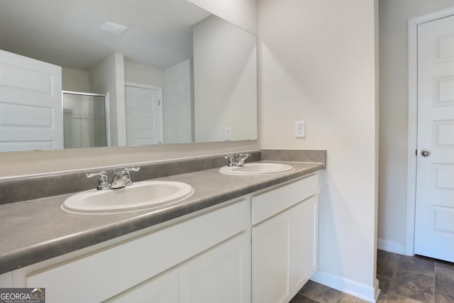 bathroom with double vanity, a sink, a shower with shower door, and baseboards