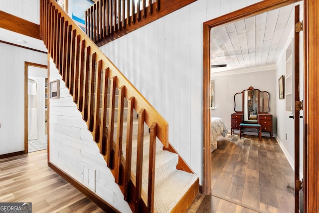 stairway with baseboards, ornamental molding, wood finished floors, and wooden walls