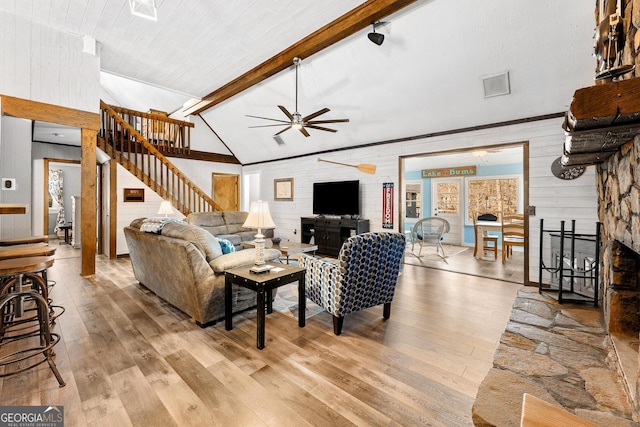 living area featuring a fireplace, stairway, lofted ceiling with beams, a ceiling fan, and wood finished floors