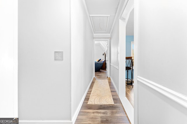 corridor featuring attic access, baseboards, and wood finished floors