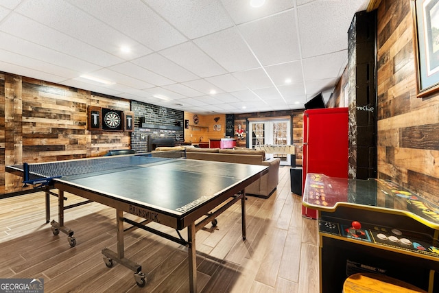 rec room featuring a paneled ceiling, wooden walls, and wood finished floors