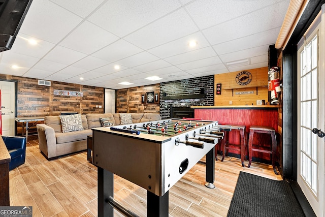 game room with a paneled ceiling, wood finished floors, visible vents, and wooden walls