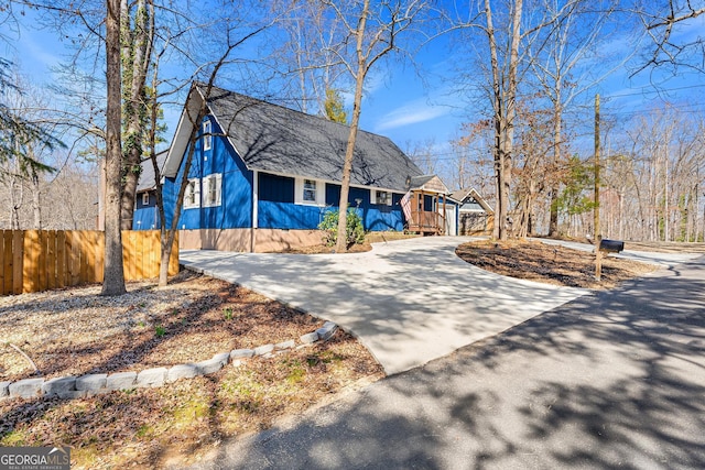 view of front facade featuring concrete driveway, roof with shingles, and fence