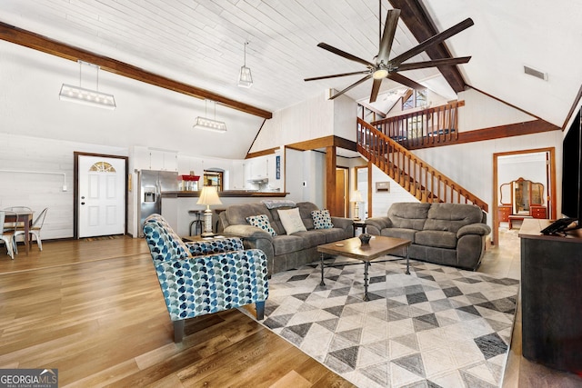 living area with stairs, high vaulted ceiling, beamed ceiling, and light wood-style flooring