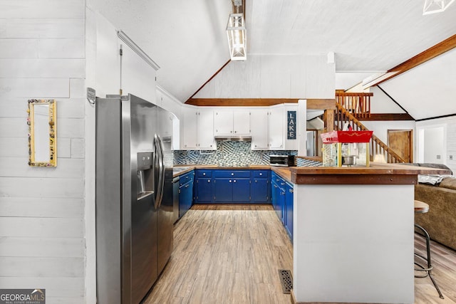 kitchen featuring lofted ceiling with beams, a peninsula, wood walls, blue cabinetry, and stainless steel fridge