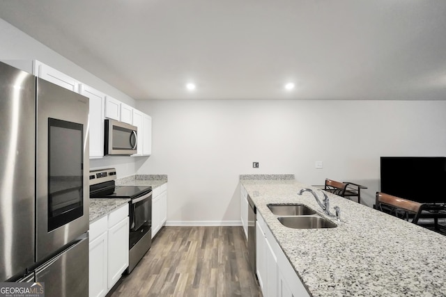 kitchen with light stone counters, wood finished floors, a peninsula, stainless steel appliances, and a sink