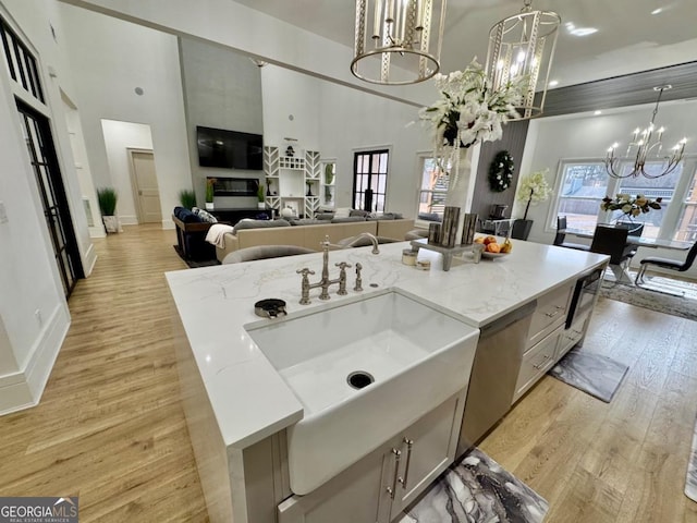 kitchen with a chandelier, an island with sink, a towering ceiling, and light wood-style floors