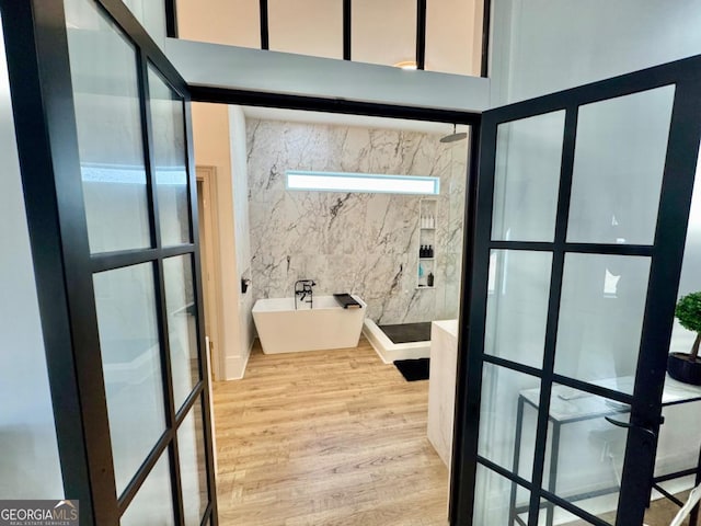 bathroom with french doors, a freestanding tub, wood finished floors, and a towering ceiling