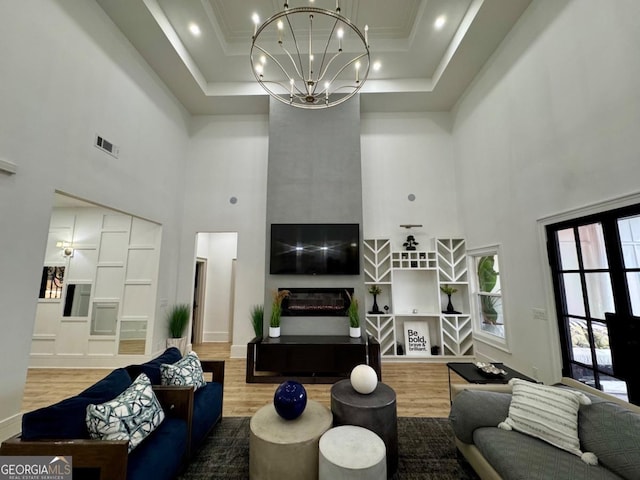 living area with a chandelier, a large fireplace, a high ceiling, wood finished floors, and visible vents