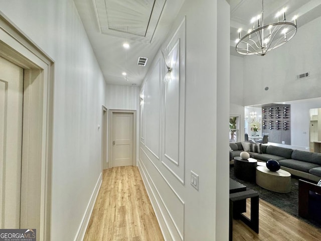 corridor with light wood-type flooring, visible vents, and a chandelier