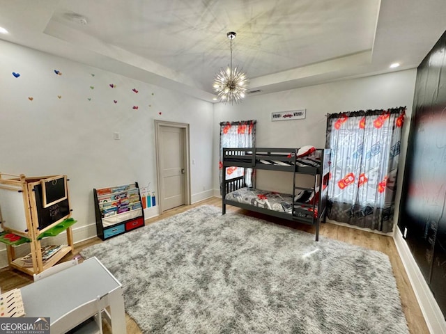 bedroom featuring a tray ceiling, visible vents, wood finished floors, a chandelier, and baseboards