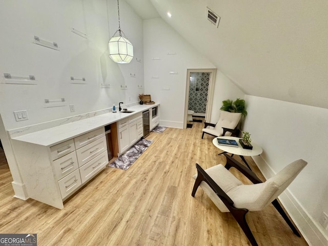 interior space with vaulted ceiling, light wood finished floors, a sink, and visible vents