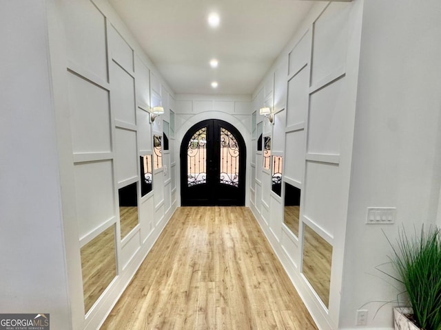 interior space with arched walkways, light wood-style flooring, french doors, a decorative wall, and recessed lighting